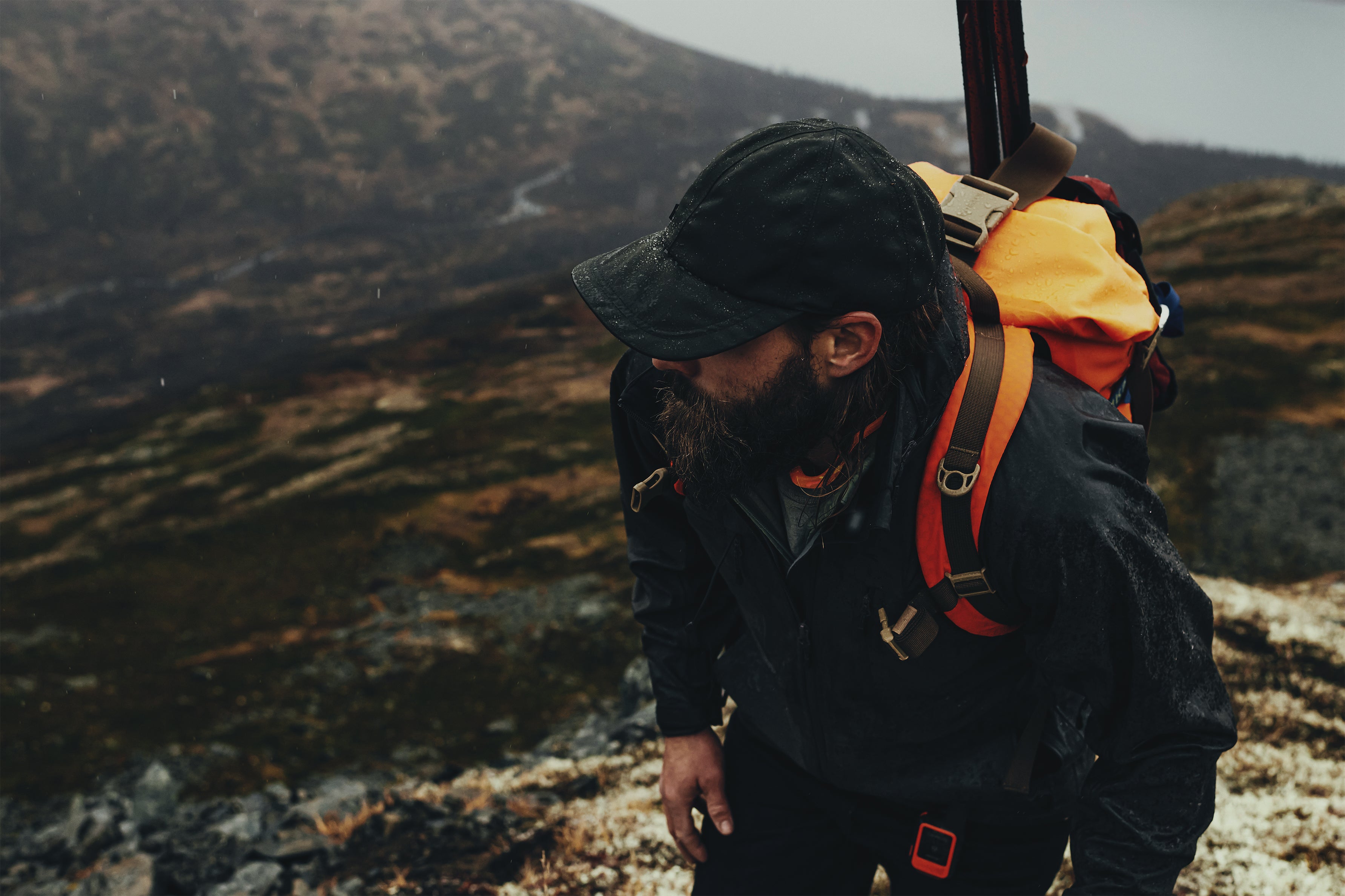 Close up of man on an outdoor hike wearing a rain jacket, cap, and orange backpack